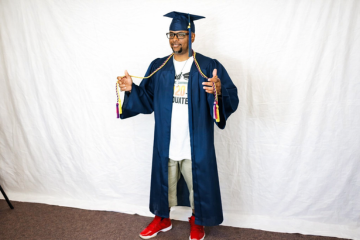 Person in graduation gown posing with Bible gesture