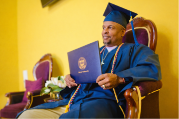 Elderly person in graduation gown reading Bible